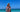 A young woman wrapped in an ECCOSOPHY microfiber beach towel called Cancun. The stripped quick dry towel is hanging off her shoulders and she is looking into the beautiful turquoise sea.